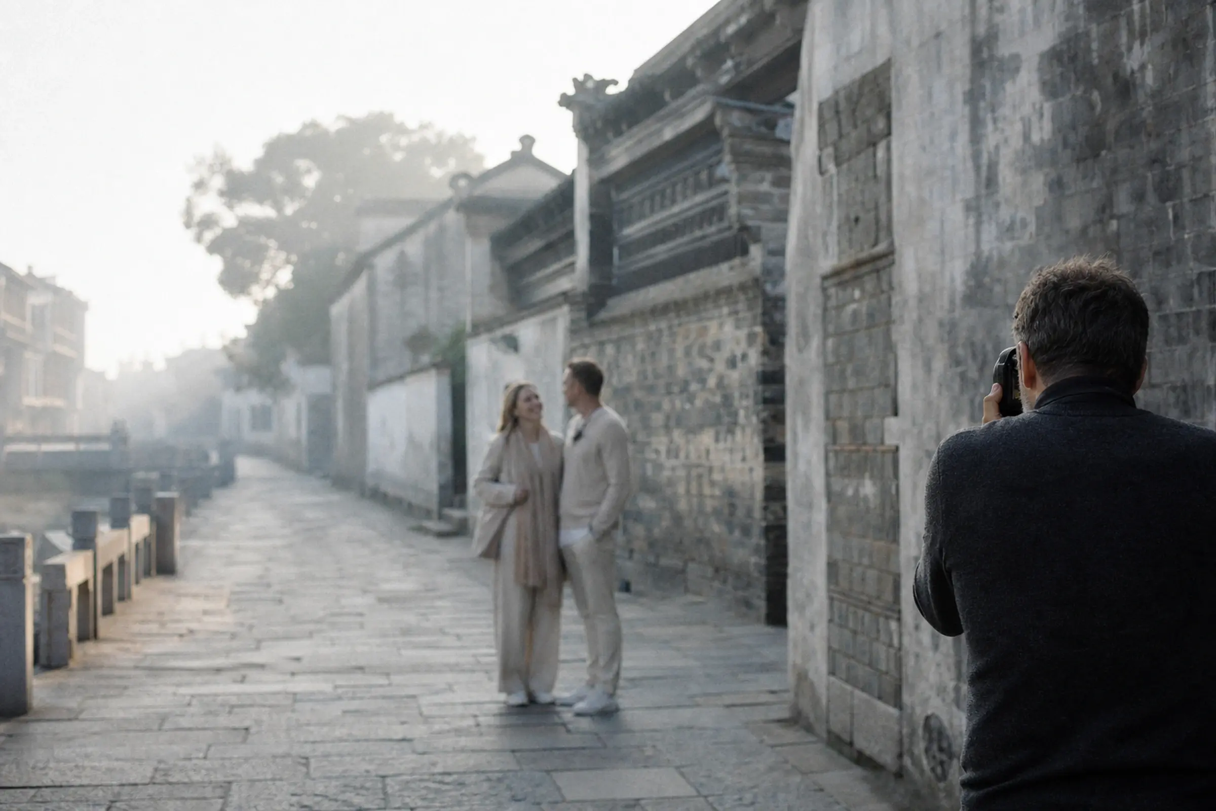 A photographer quietly filming a couple in a misty stone lane
