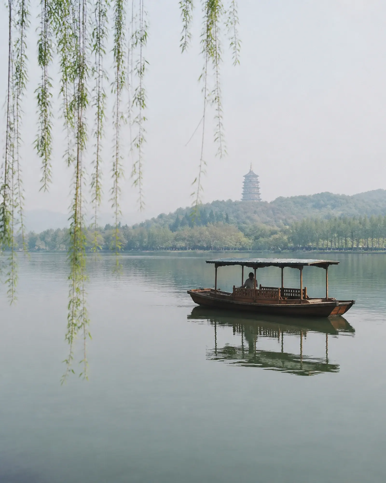 A lone boat on West Lake at dawn, mist softening the hills and a pagoda on the far shore
